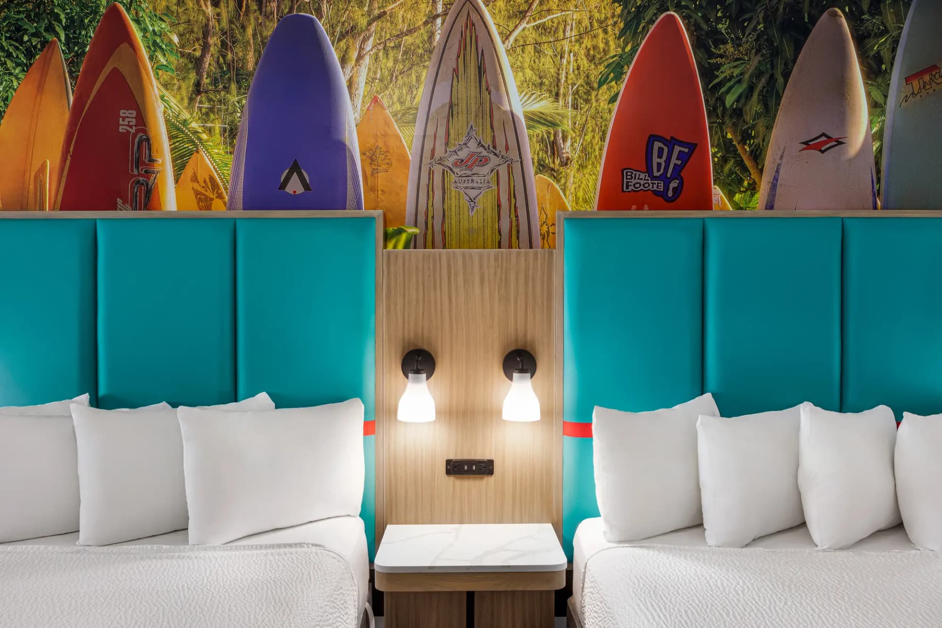 Two queen beds with teal headboards under a surfboard mural